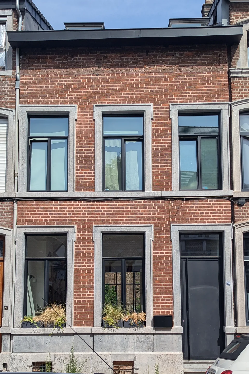 Photo de départ : façade en briques rouges, trois fenêtres à l’étage, deux fenêtres et une porte anthracite à droite, sous une corniche sombre